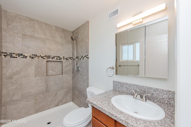 bathroom with visible vents, a tile shower, vanity, and toilet