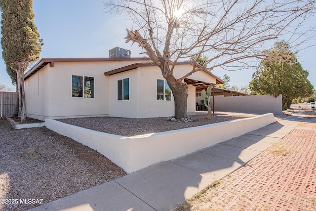 view of front facade with central air condition unit, fence, and stucco siding