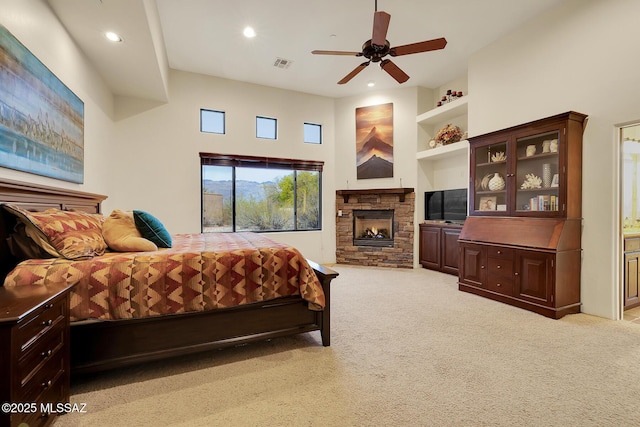 carpeted bedroom with ceiling fan, a stone fireplace, and ensuite bath