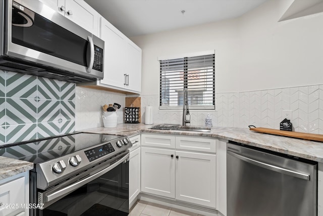 kitchen with tasteful backsplash, light stone countertops, stainless steel appliances, white cabinetry, and a sink