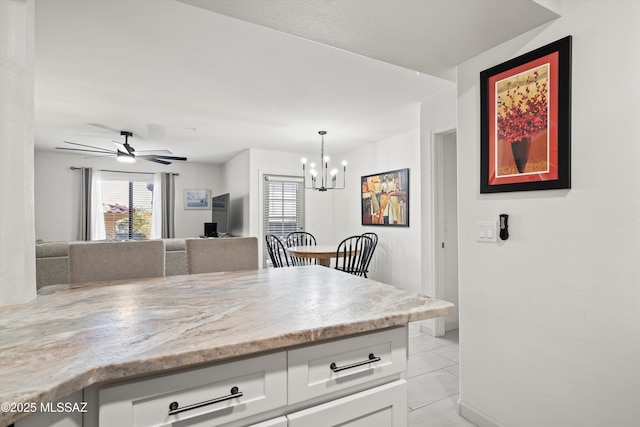 kitchen featuring ceiling fan with notable chandelier, white cabinets, open floor plan, hanging light fixtures, and light stone countertops