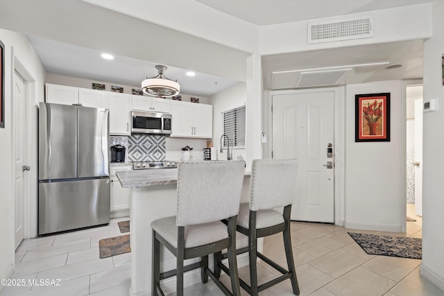 kitchen with visible vents, white cabinets, decorative backsplash, stainless steel appliances, and a kitchen bar