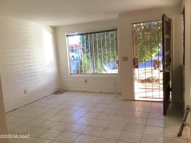 spare room featuring light tile patterned floors and brick wall