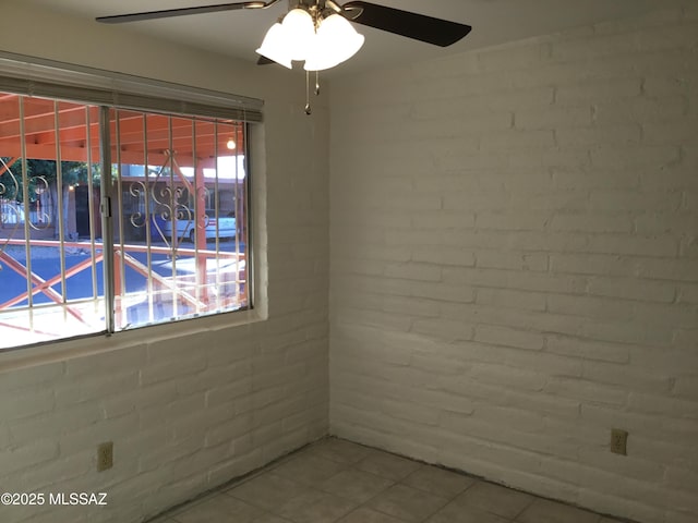 tiled empty room featuring ceiling fan and brick wall