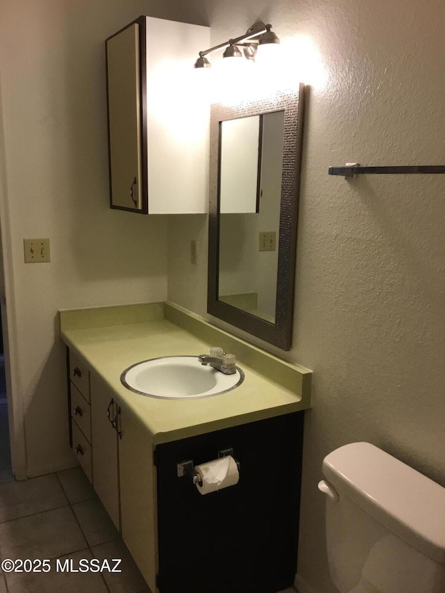 half bathroom featuring tile patterned flooring, a textured wall, vanity, and toilet