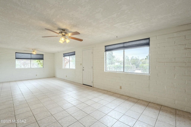 spare room with light tile patterned flooring, ceiling fan, a textured ceiling, and brick wall