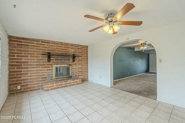 unfurnished living room with arched walkways, a fireplace, light tile patterned floors, a ceiling fan, and light carpet