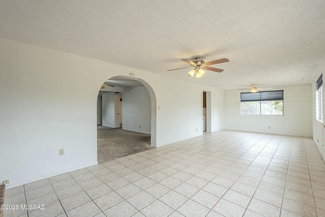 unfurnished room with a ceiling fan, light tile patterned floors, arched walkways, and a textured ceiling