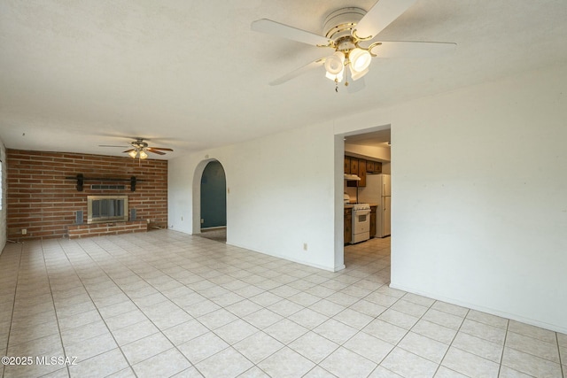 unfurnished living room featuring light tile patterned floors, ceiling fan, a fireplace, and arched walkways