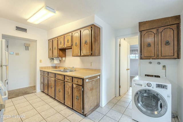 kitchen with washer / clothes dryer, a sink, light countertops, backsplash, and light tile patterned flooring