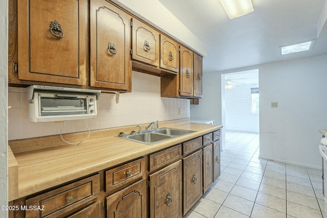 kitchen with light tile patterned floors, baseboards, decorative backsplash, light countertops, and a sink