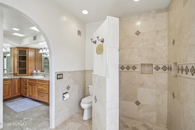 bathroom featuring tile patterned flooring, toilet, a tile shower, tile walls, and vanity