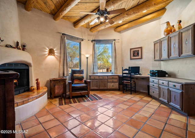 home office with a fireplace with raised hearth, wood ceiling, beam ceiling, light tile patterned floors, and built in study area