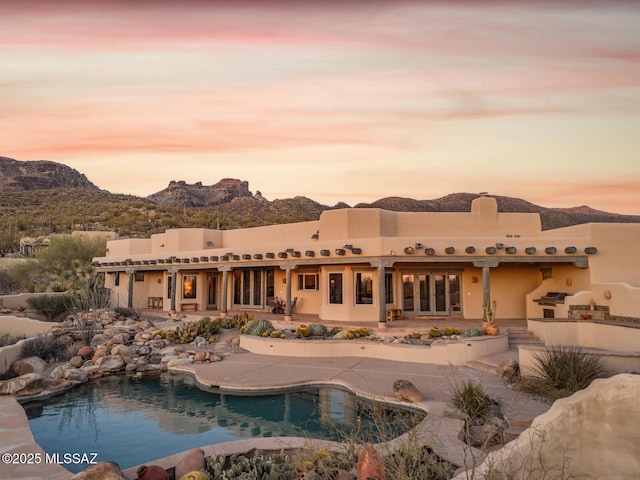 rear view of house with a patio area, an outdoor pool, a mountain view, and french doors