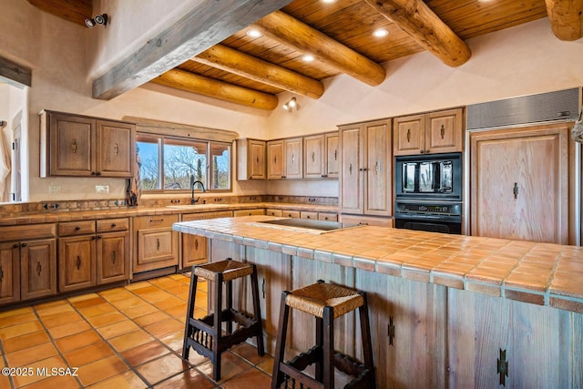 kitchen with black appliances, a sink, a breakfast bar area, wooden ceiling, and tile counters