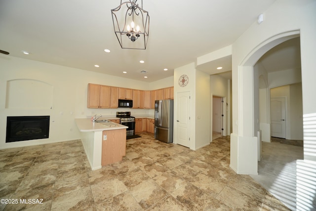 kitchen featuring stainless steel appliances, a peninsula, a sink, light countertops, and a glass covered fireplace