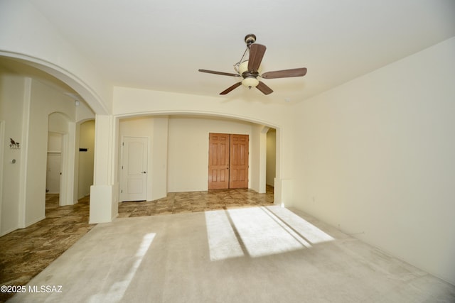 carpeted empty room with arched walkways and ceiling fan