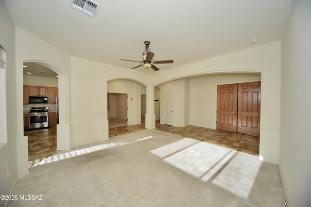 unfurnished room featuring light colored carpet, visible vents, ceiling fan, and arched walkways