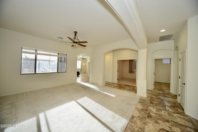 spare room featuring carpet, visible vents, arched walkways, and ceiling fan