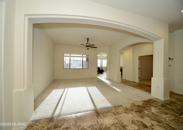 interior space with arched walkways, stone finish flooring, and ceiling fan