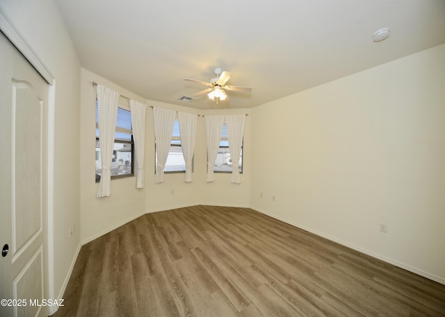 spare room with a ceiling fan, visible vents, baseboards, and wood finished floors