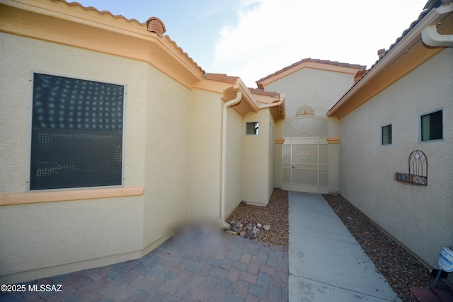 exterior space with a gate, a tiled roof, and stucco siding