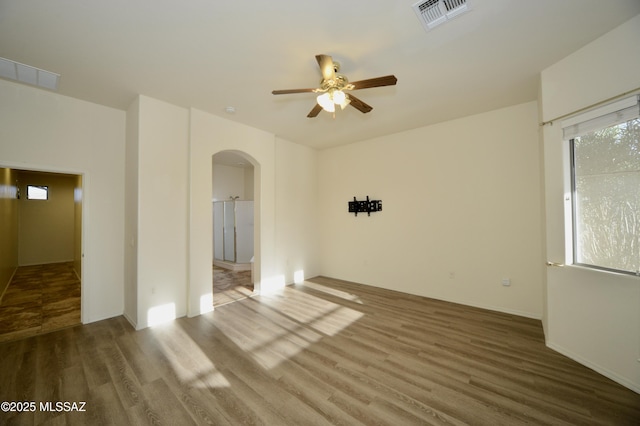 unfurnished room with a ceiling fan, arched walkways, visible vents, and wood finished floors