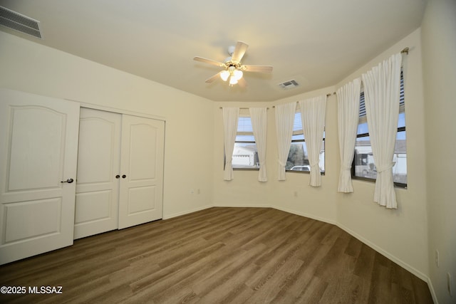 unfurnished bedroom with a closet, wood finished floors, visible vents, and baseboards