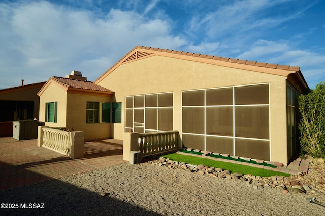 rear view of property featuring a patio area, a tile roof, a sunroom, and stucco siding