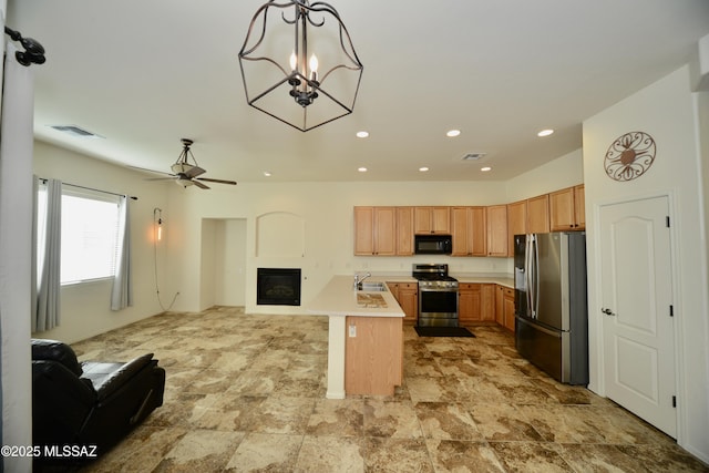 kitchen with light countertops, appliances with stainless steel finishes, a glass covered fireplace, open floor plan, and a sink