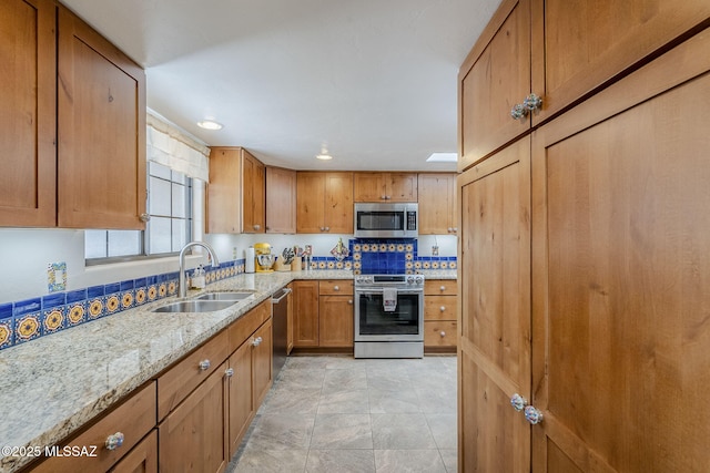 kitchen with light tile patterned floors, light stone counters, a sink, appliances with stainless steel finishes, and brown cabinets