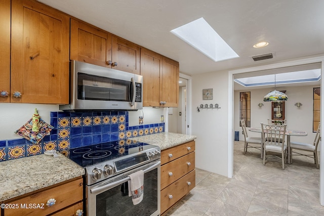 kitchen with stainless steel appliances, brown cabinets, decorative light fixtures, and light stone countertops