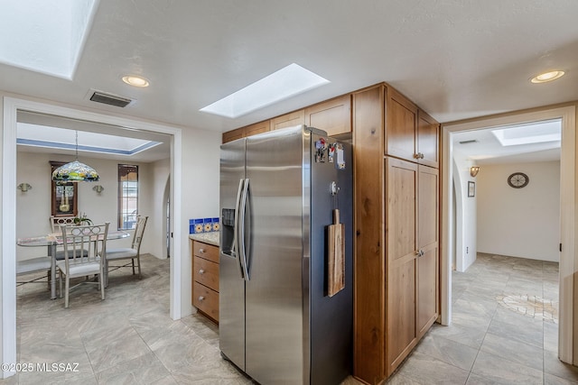 kitchen featuring a skylight, visible vents, hanging light fixtures, brown cabinetry, and stainless steel fridge