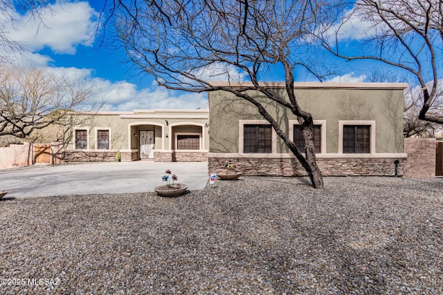 pueblo-style house with stone siding, fence, and stucco siding