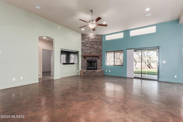 unfurnished living room featuring arched walkways, a ceiling fan, a high ceiling, concrete floors, and a fireplace