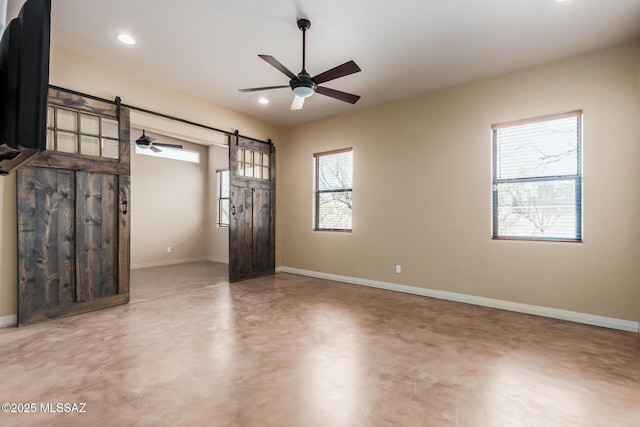 unfurnished room with a barn door, concrete floors, and baseboards