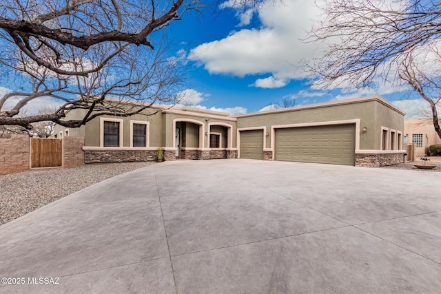 pueblo revival-style home featuring a garage, stone siding, and stucco siding