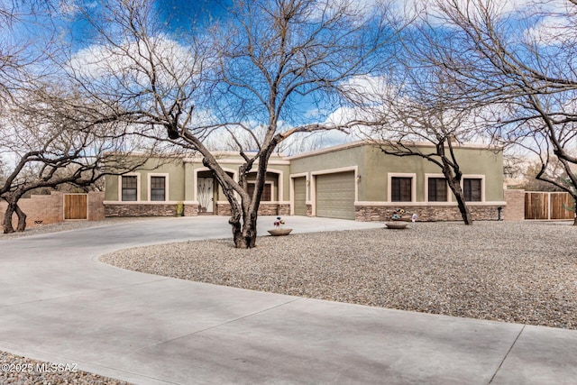 adobe home with an attached garage, fence, stone siding, concrete driveway, and stucco siding