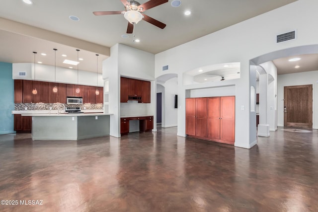 unfurnished living room with finished concrete flooring, visible vents, arched walkways, a towering ceiling, and ceiling fan