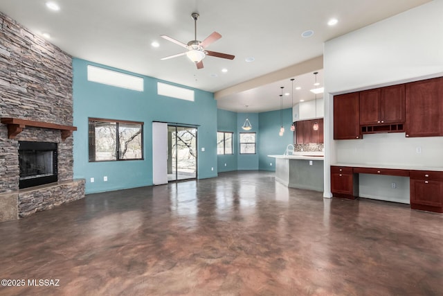 unfurnished living room with a towering ceiling, built in study area, ceiling fan, a stone fireplace, and concrete flooring