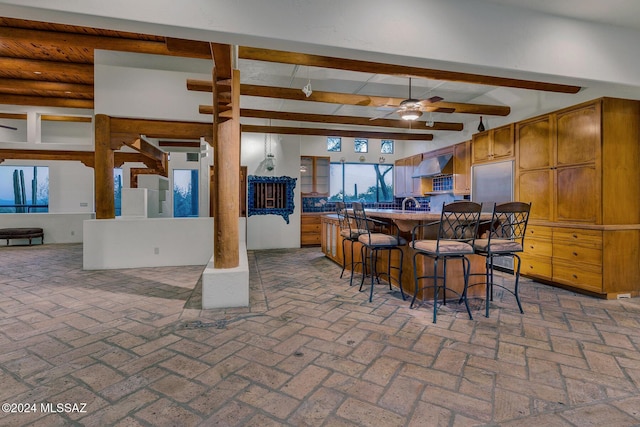 kitchen with a breakfast bar, sink, ceiling fan, beam ceiling, and wall chimney exhaust hood