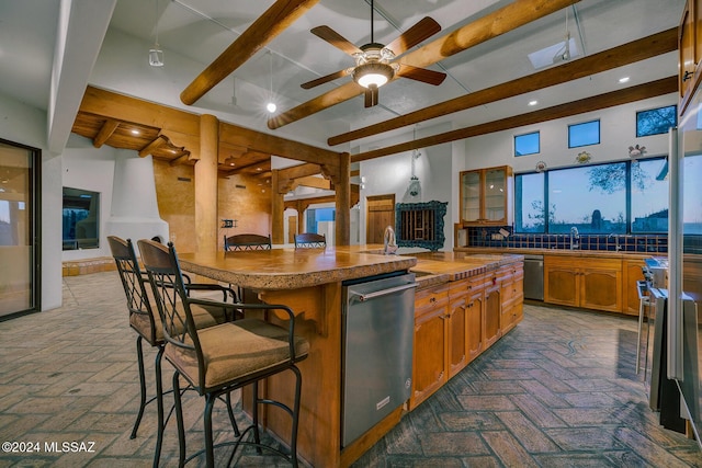 kitchen with dishwasher, a kitchen breakfast bar, ceiling fan, a center island with sink, and beam ceiling