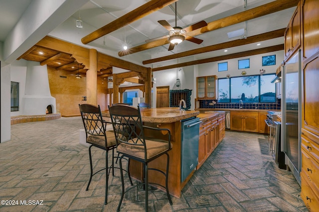 kitchen with a kitchen bar, a kitchen island with sink, ceiling fan, stainless steel appliances, and beam ceiling