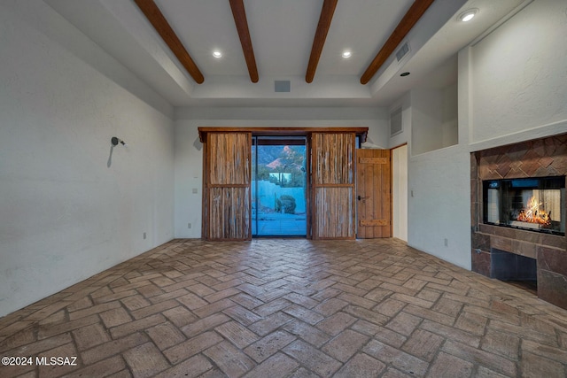 unfurnished living room featuring a towering ceiling, beam ceiling, and a tile fireplace