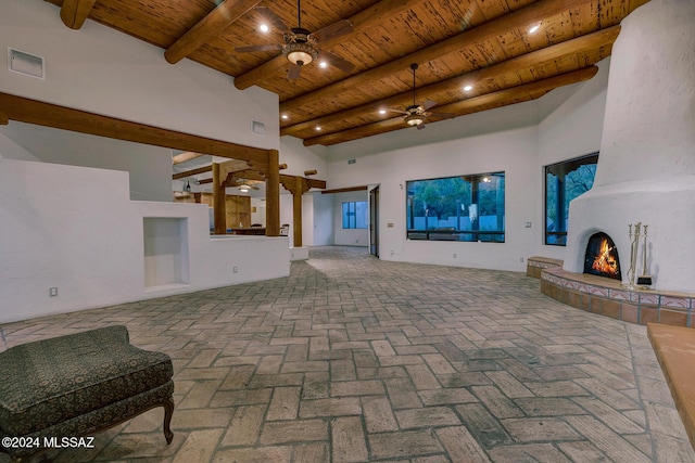 unfurnished living room with wood ceiling, ceiling fan, a fireplace, and a high ceiling