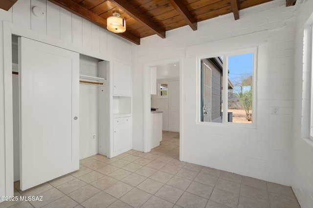 unfurnished bedroom featuring a closet, wooden ceiling, light tile patterned flooring, and beamed ceiling