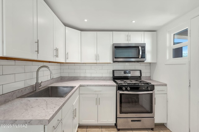 kitchen with light tile patterned floors, decorative backsplash, appliances with stainless steel finishes, white cabinetry, and a sink