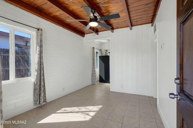 spare room with beam ceiling, wood ceiling, light tile patterned flooring, ceiling fan, and brick wall