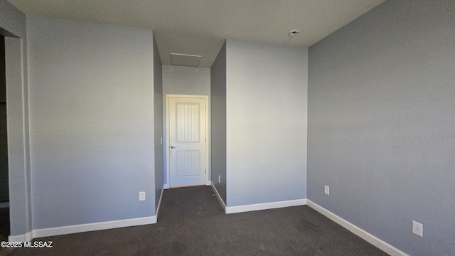 empty room featuring dark colored carpet, baseboards, and attic access