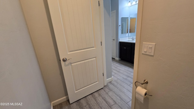 hall featuring baseboards, light wood-type flooring, and a sink